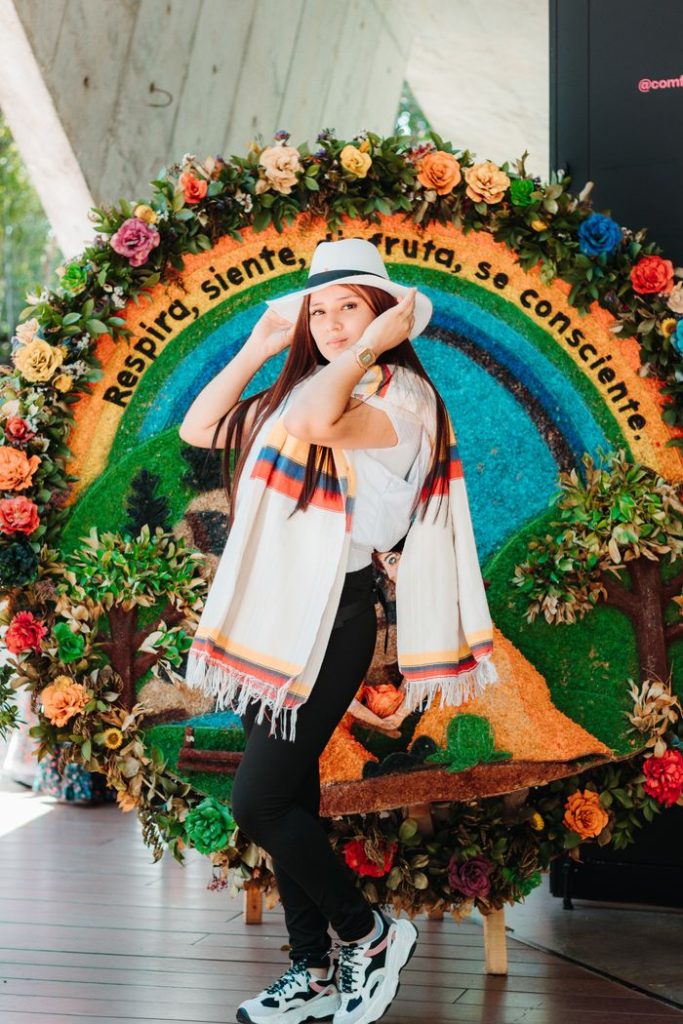 woman-wearing-a-hat-and-a-scarf-18357986 Woman in traditional Colombian attire posing with floral art background in Santa Elena.